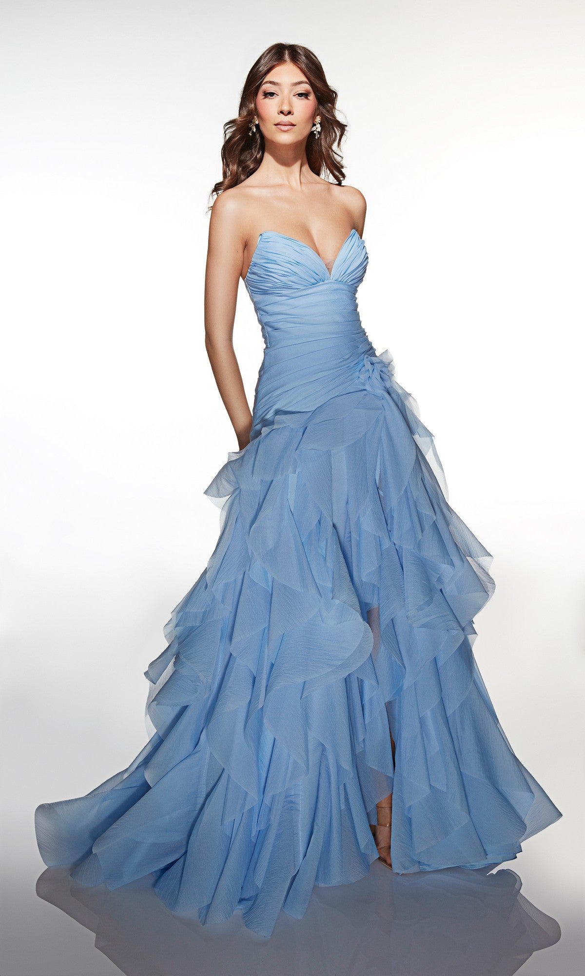 A woman stands against a plain white background wearing the Alyce 62024 Long Prom Dress, a floor-length light blue gown with delicate ruffles.
